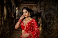 Beautiful Indian woman in a red saree with jewelry, posing in an ancient building setting.